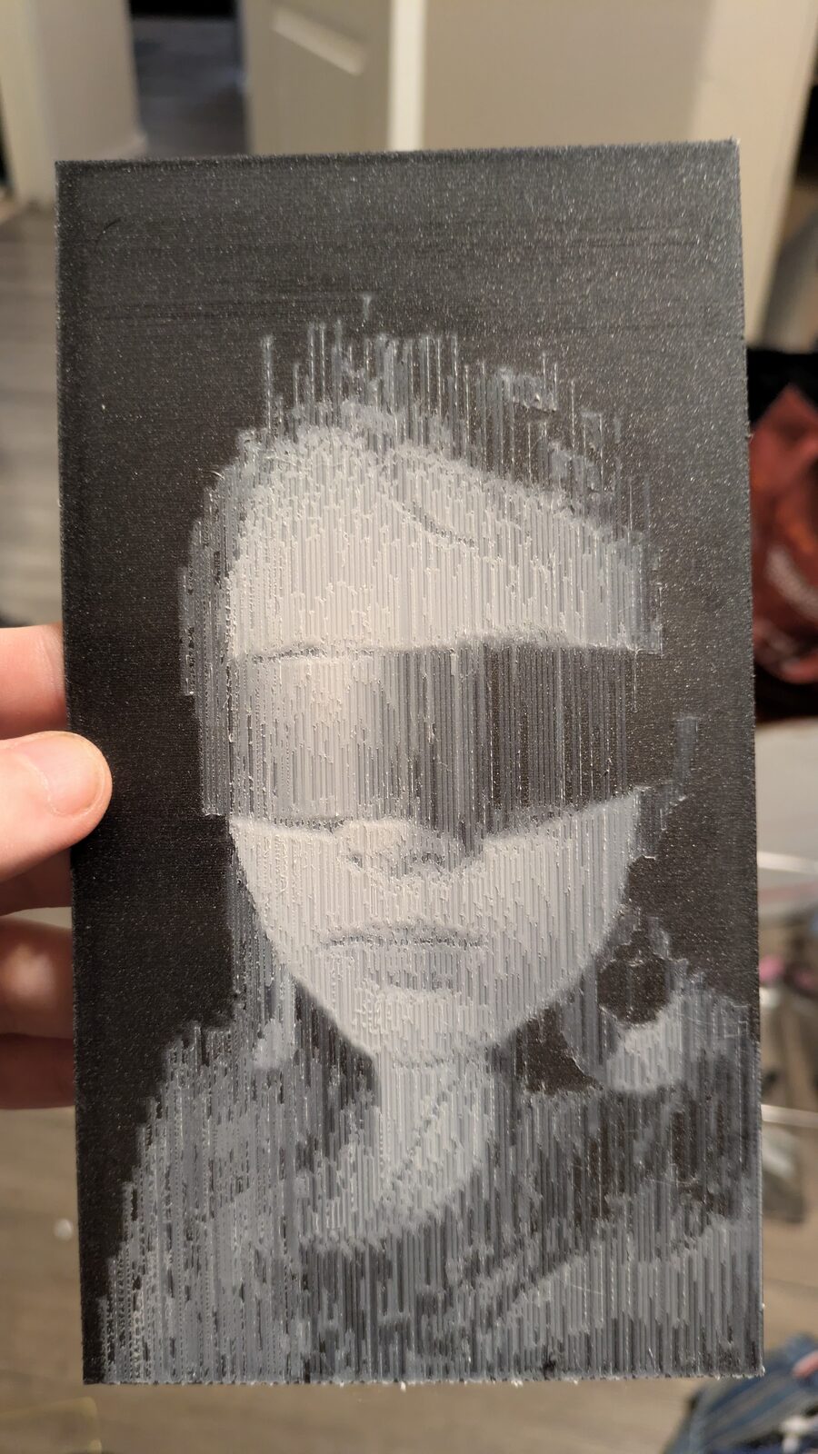 A 3D-printed portrait held in a hand: a girl in a mirrored visor, drawn in fine vertical white lines on black